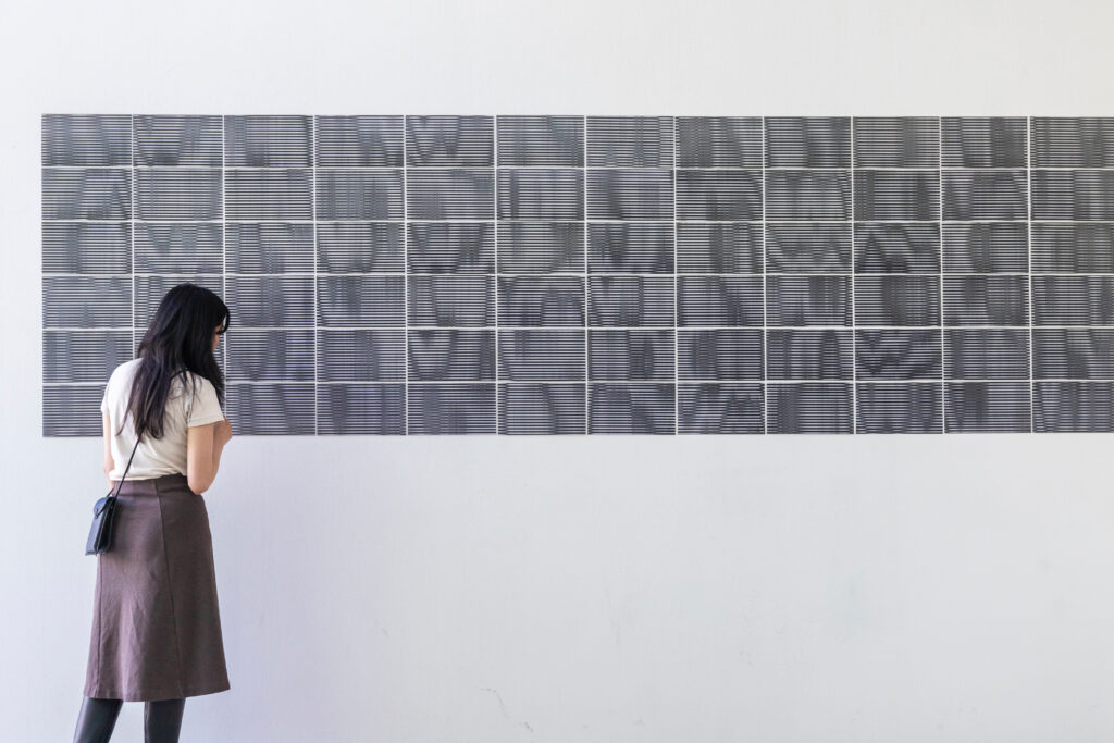 Gesamtansicht eines lentikularen Drucks im Raum, montiert als rechteckige Wandarbeit mit kontrastreichen schwarz-weißen Streifen. Kino Siska Ljublijana